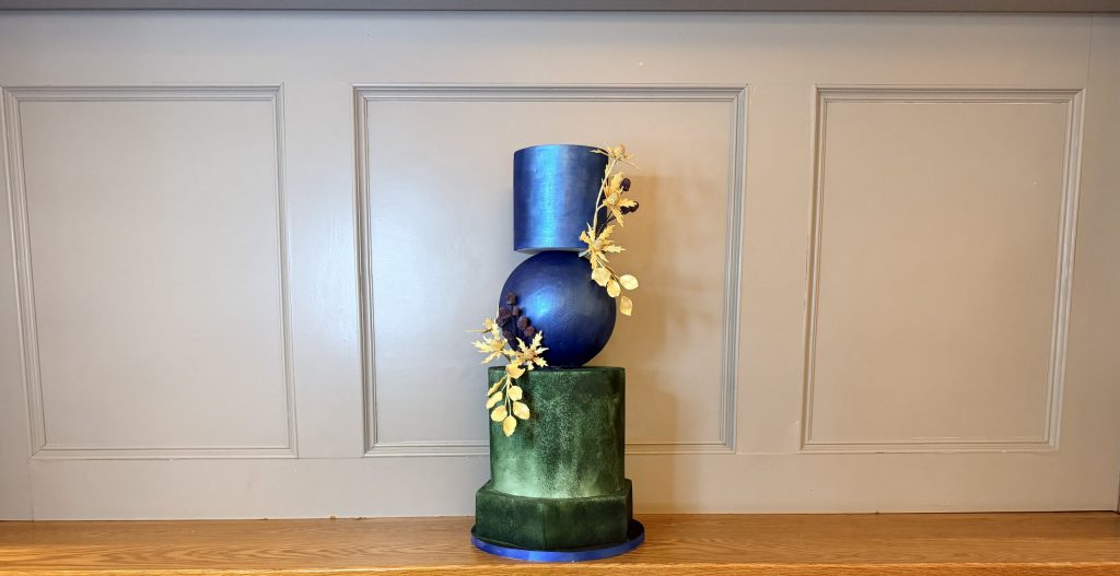 Architectural wedding cake installation featuring metallic blue sphere and forest green tiers for luxury Scottish industrial venues.