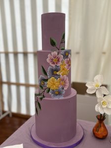 bespoke three-tier wedding cake in deep lilac with hand-painted botanical floral artistry, designed as a premium sculptural commission for a luxury estate wedding in the Scottish Borders.