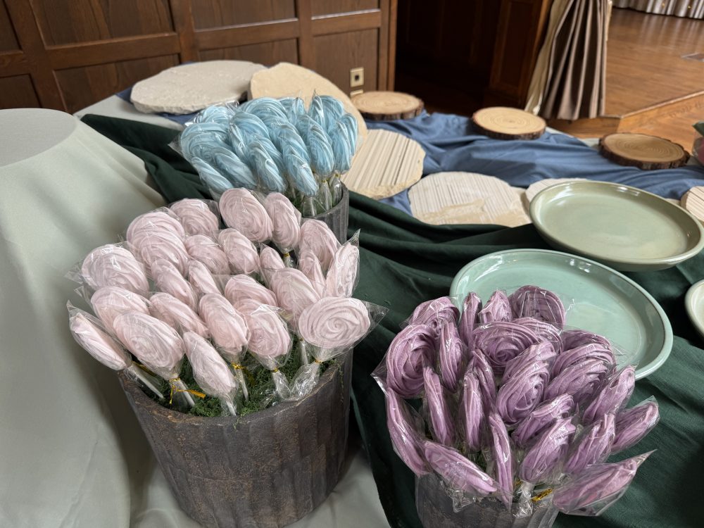 Pastel meringue lollipops arranged in artisanal vessels as part of a luxury wedding dessert table in Scotland by Crumbdidilyumptious.