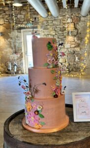Pink wedding cake decorated with fresh edible flowers and piped flowers