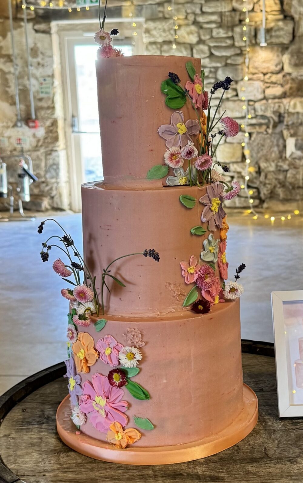 Pink wedding cake decorated with fresh edible flowers and piped flowers